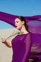 Amazing beautiful brunette woman with the Peacock feather in purple fabric in the desert. Oriental, indian, fashion, style concept photo