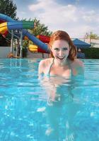 Portrait of smiling young beautiful redhead woman in sunny day in open swimming pool in summer photo