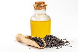 Sesame oil in glass bottle with black sesame seed in wooden scoop on white photo
