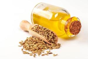 Essential oil in a bottle with fennel seeds in scoop and scattered on white background photo