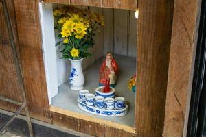 Buddhist Shrine with Flowers, Liquor in Ceramic Cups and a Small Statue of the God of Money at a Cafe in Vietnam