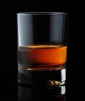 Scotch whiskey in an elegant glass on a black background with reflections.
