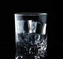 Ice cubes in empty glass on black background. Glass of water or whiskey and wine. Empty glass for alcoholic beverages photo