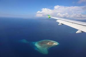 avión volando sobre el mar azul profundo con una foto de la isla a través del avión de la ventana