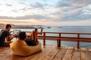 Two young man relaxing on bean bag at balcony with ocean view photo