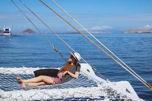 Woman in summer hat and sunglasses relaxing on catamaran net enjoying sea view photo