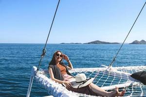 Smiling asian woman wearing sunglasses relaxing on catamaran net enjoying summer holiday photo