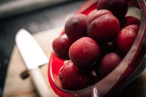 Red plums on bread board with knife and black background photo