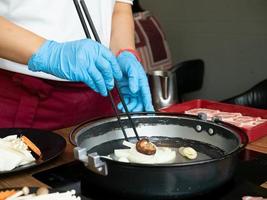 chef restaurante cocina usar guante máscara azul está cocinando palillos shabu suki buffet saludable vegetal cerdo mariscos carne de vaca cliente asiático japonés coreano china comer cálido caliente para proteger covid-19 enfermedad foto