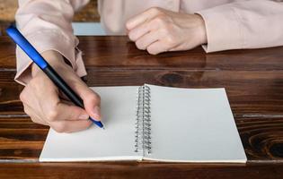 Close up of woman holding a pen for writing something or message on empty white paper in an opened book.