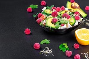 Vegetable salad with avocado, greens, onion micro-greens and raspberries on a black background photo