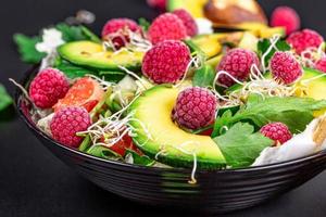 Close-up, salad with avocado and raspberries in a black bowl. The concept of vitamins, taking care of the figure photo