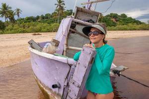 dama posando junto a un viejo barco de pesca abandonado y medio hundido en praia dos nativos, en trancoso, bahia, brasil foto
