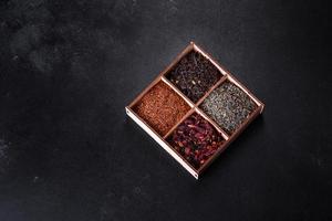 Several kinds of dry black tea with bergamot, rooibos, green and frame in a wooden box on a black concrete background photo