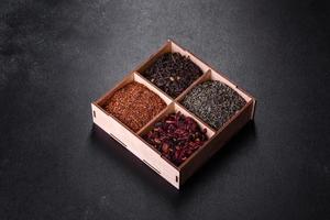 Several kinds of dry black tea with bergamot, rooibos, green and frame in a wooden box on a black concrete background photo