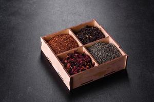 varios tipos de té negro seco con bergamota, rooibos, verde y marco en una caja de madera sobre un fondo de hormigón negro foto