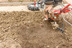 Small farm tractor plows the ground, the work of a walk-behind tractor photo