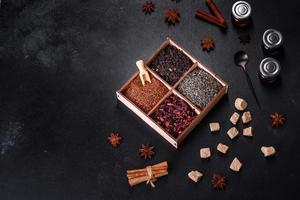 Several kinds of dry black tea with bergamot, rooibos, green and frame in a wooden box on a black concrete background photo