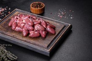 corazones de pollo crudos sin cocer en una tabla de cortar de madera sobre una mesa de hormigón oscuro