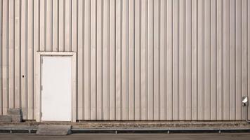 la antigua puerta blanca en la pared de chapa metálica del almacén o edificio de fábrica con tubería en suelo de hormigón foto