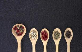 Flat lay of various colors peppercorns in wooden spoon on black stone slate background photo