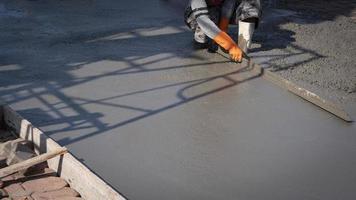 Cropped image of Asian construction worker using long triangle trowel to plastering cement on the floor in construction site photo