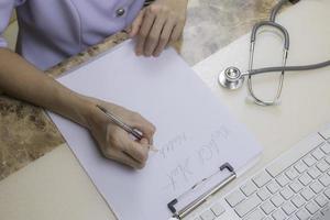 High angle view of Asian female doctor or nurse is writing prescription with stethoscope and part of computer keyboard on the table at hospital office room