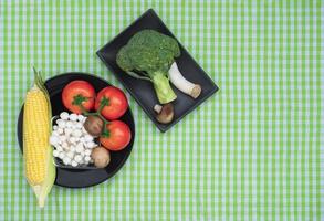 Top view of various fresh vegetables in black plates on green plaid tablecloth photo