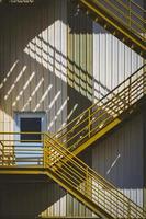luz solar y sombra en la superficie de la escalera de incendios amarilla fuera del antiguo edificio industrial en marco vertical foto