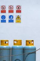 tanques de cilindros de gas con varias señales de advertencia en la pared de cemento blanco en el área de la zona de seguridad foto