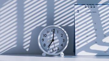 Sunlight and shadow on surface of white round table clock with 2021 desk calendar on white table at morning time photo