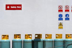 Gas cylinder tanks with safety first label and various warning signs on white cement wall background