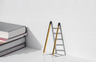Two pencils and shadow in form of ladder with stack of textbooks on white tabletop, Education, learning is the ladder to success concept