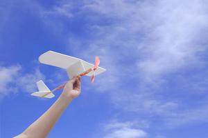 Child hand holding rubber powered aircraft up in the air against blue sky background photo