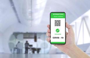 Man hand showing health passport of vaccination certification on smartphone with blurred background of arrival or departure screening checkpoint at airport photo