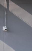 Sunlight and shadow on surface of security camera with flexible metal conduit on gray cement wall in vertical frame photo