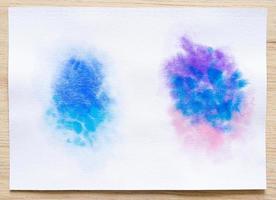 Colorful watercolor brush strokes on white paper sheet with wood background. photo