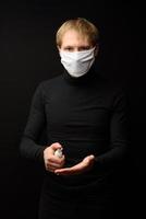 A portrait of man with medical face mask using disinfectant spray on hands. People, medicine and healthcare concept. Coronavirus protection photo