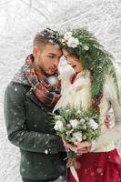 Beautiful bride and groom with a white dog are standing on the background of a snowy forest. photo