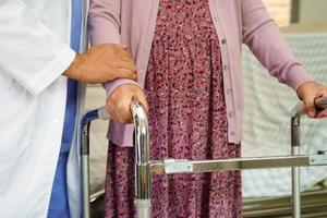 Doctor help Asian elderly woman disability patient walk with walker in nursing hospital, medical concept. photo