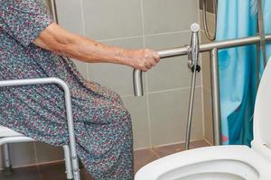 una anciana asiática usa un riel de soporte para el inodoro en el baño, barra de seguridad para pasamanos, seguridad en el hospital de enfermería. foto