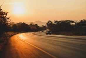 Country road with moving cars and beautiful golden sunset background in Thailand.
