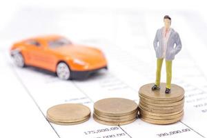 Miniature businessman and stack coins on statement and the car behind. saving and loan concept. photo