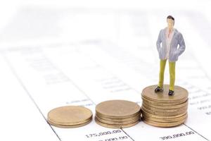 Miniature businessman and stack coins on statement photo