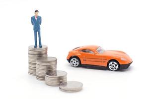 Miniature businessman standing on coins and the car behind. saving and loan concept. photo