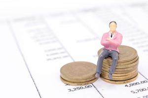 Miniature businessman and stack coins on statement photo