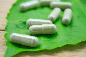 Cápsulas de hierbas medicinales con hoja de hierba verde sobre mesa de madera foto