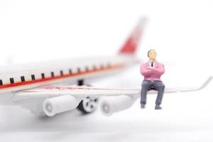 Miniature businessman sitting on airplane wing on white background photo