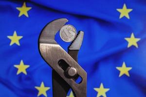 Coin one ruble is clamped in a wrench against the background of the flag of European Union. The idea of the collapse of the ruble and economy sanctions against Russia. photo