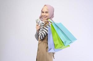 Young beautiful muslim woman in suit holding colorful shopping bags over white background studio photo